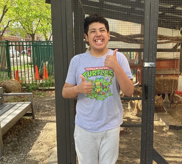 Child smiling and offering thumbs up in front of chicken coop