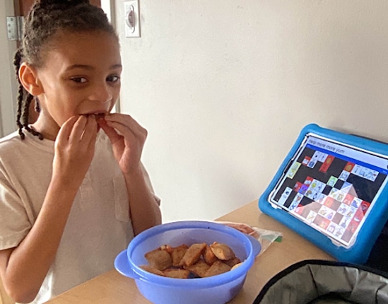 child eating a snack at a table next to an aac device