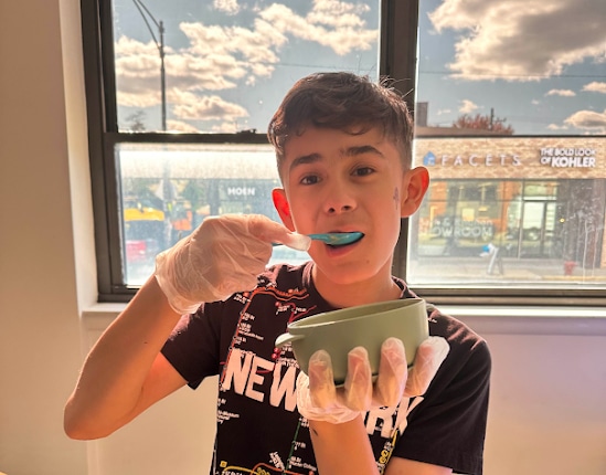 child holding a bowl and eating something out of it with a spoon